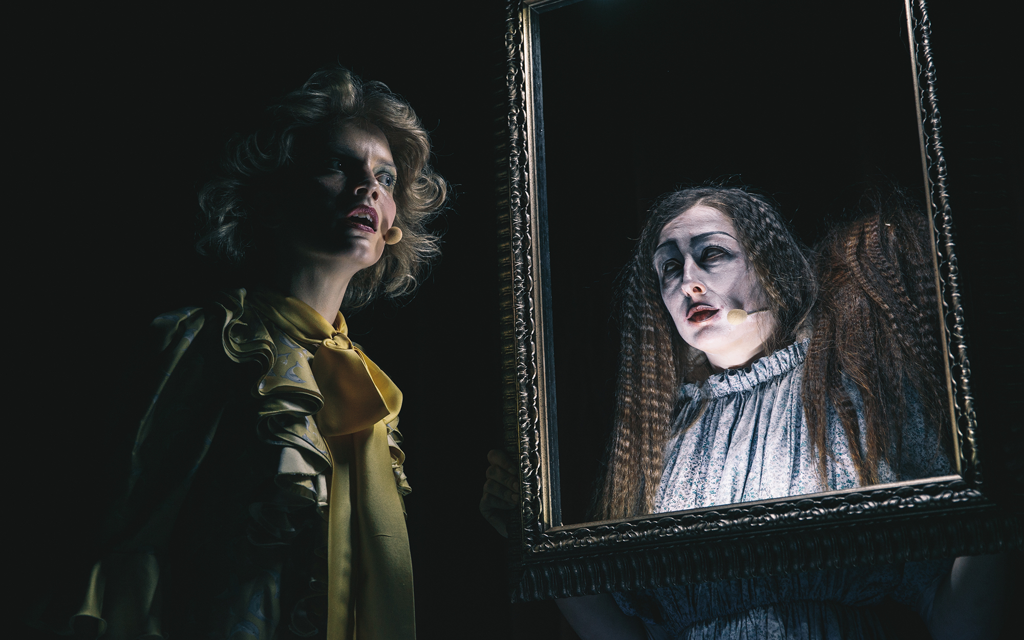 Alenka Krneki (Barbara Ribnikar) začudena stoji pred okvirjem slike, za okvirjem je Prednica Addams (Sara Gorše). Avtor fotografije: Peter Giodani. 