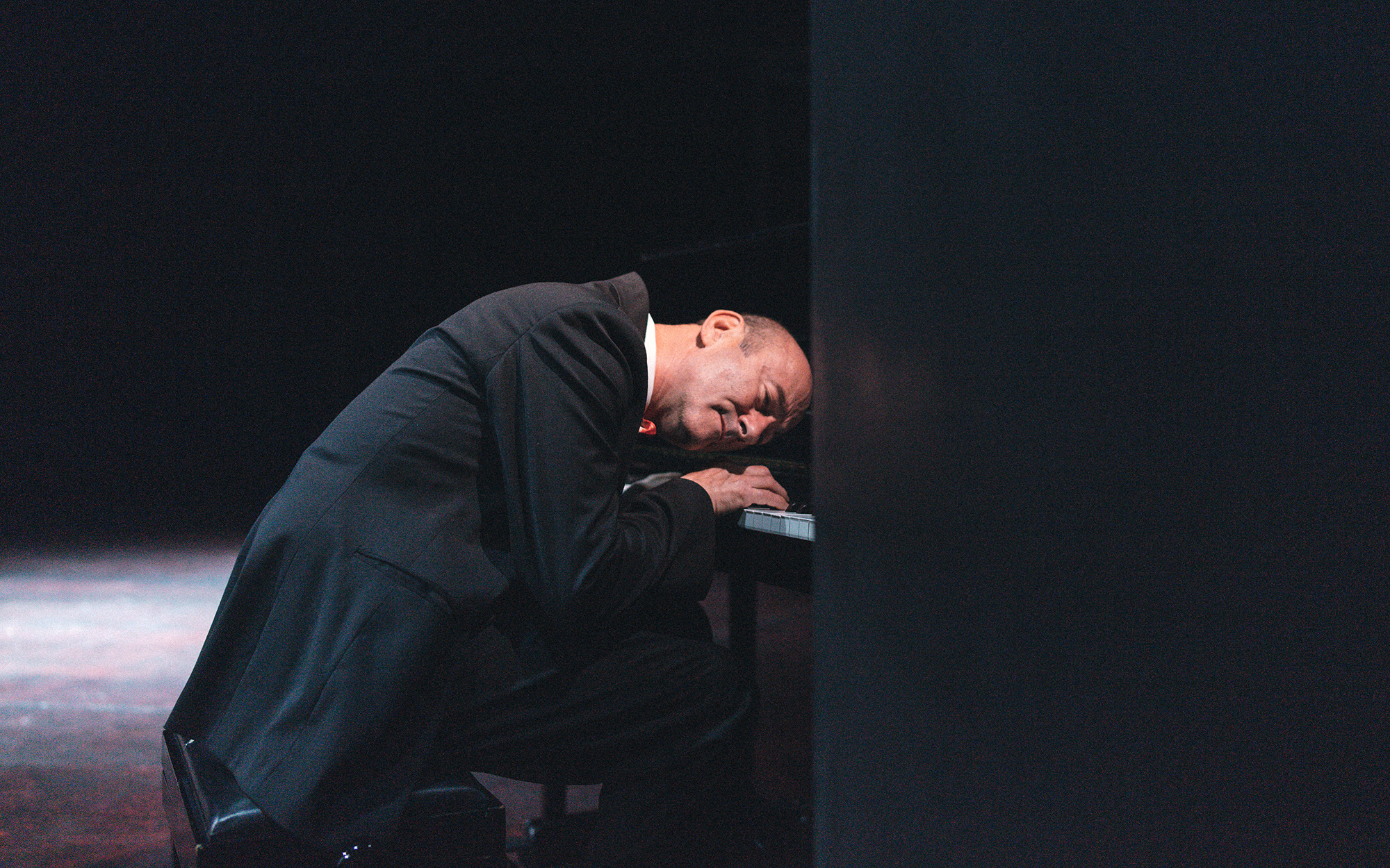 Firs (Boris Ostan) igra na pianino, z glavo je prislonjen h klaviaturi, kot da prisluškuje tipkam.