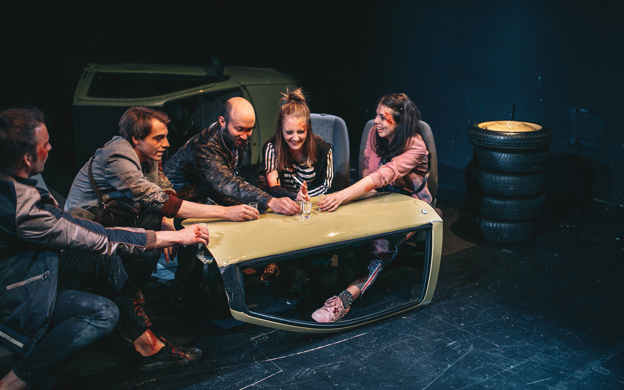 Peter (Filip Samobor), Žan (Matic Lukšič), Dejan (Tines Špik), Leni (Lena Hribar Škrlec) in Viktorija (Anuša Kodelja) si nasmejani nazdravljajo. Sedijo ob provizorični mizici iz avtomobilskih vrat, na njej so steklenica žganja in kozarčki. Avtor fotografi