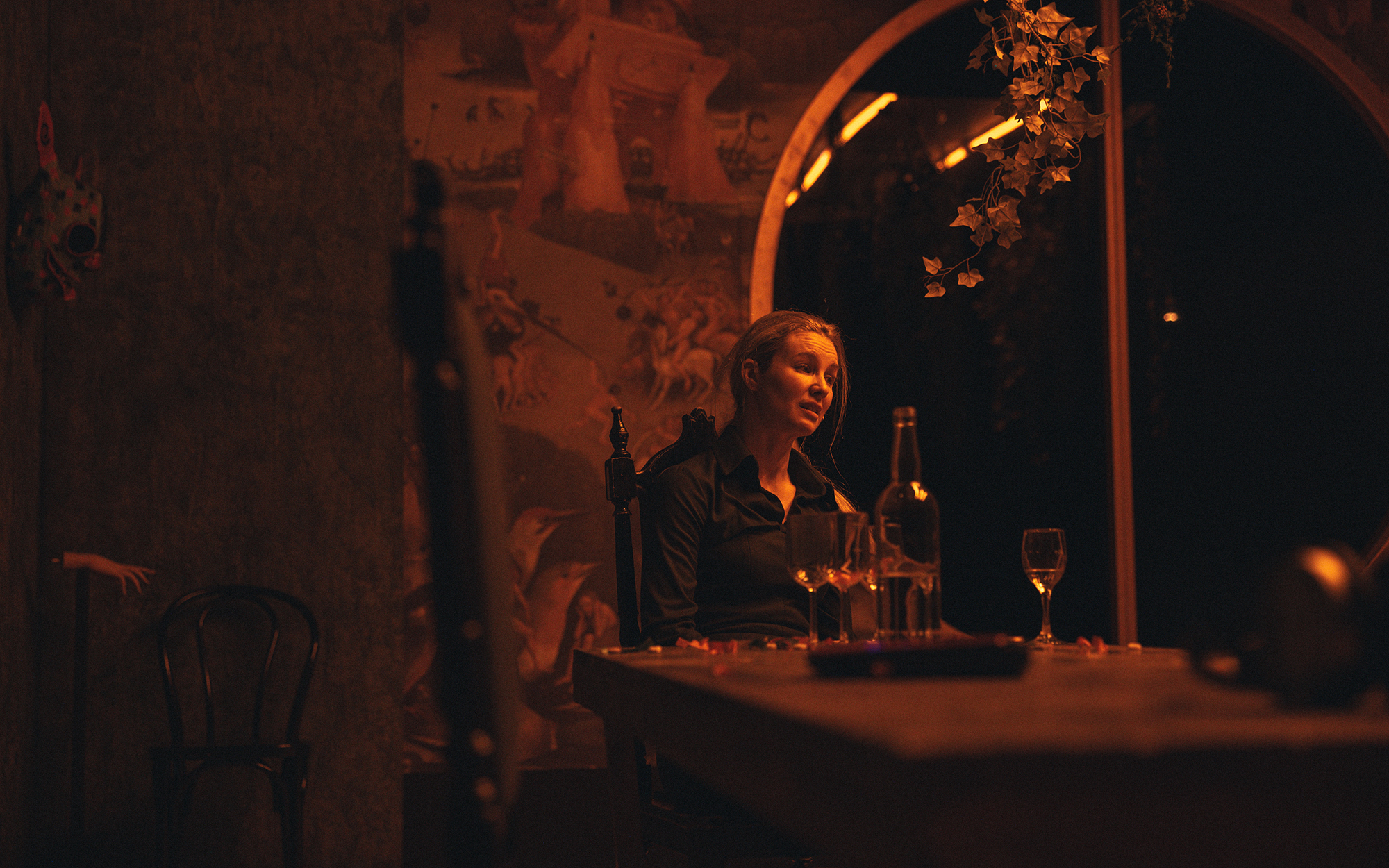 Ženska (Iva Krajnc Bagola) sedi za jedilno mizo, na kateri je nekaj kozarcev, pa tudi steklenica, prenosni računalnik, slušalke in konfeti. Videti je obupana, nekaj žalostno razlaga. V ozadju je veliko stekleno okno, s stropa visi nekaj zelenja.