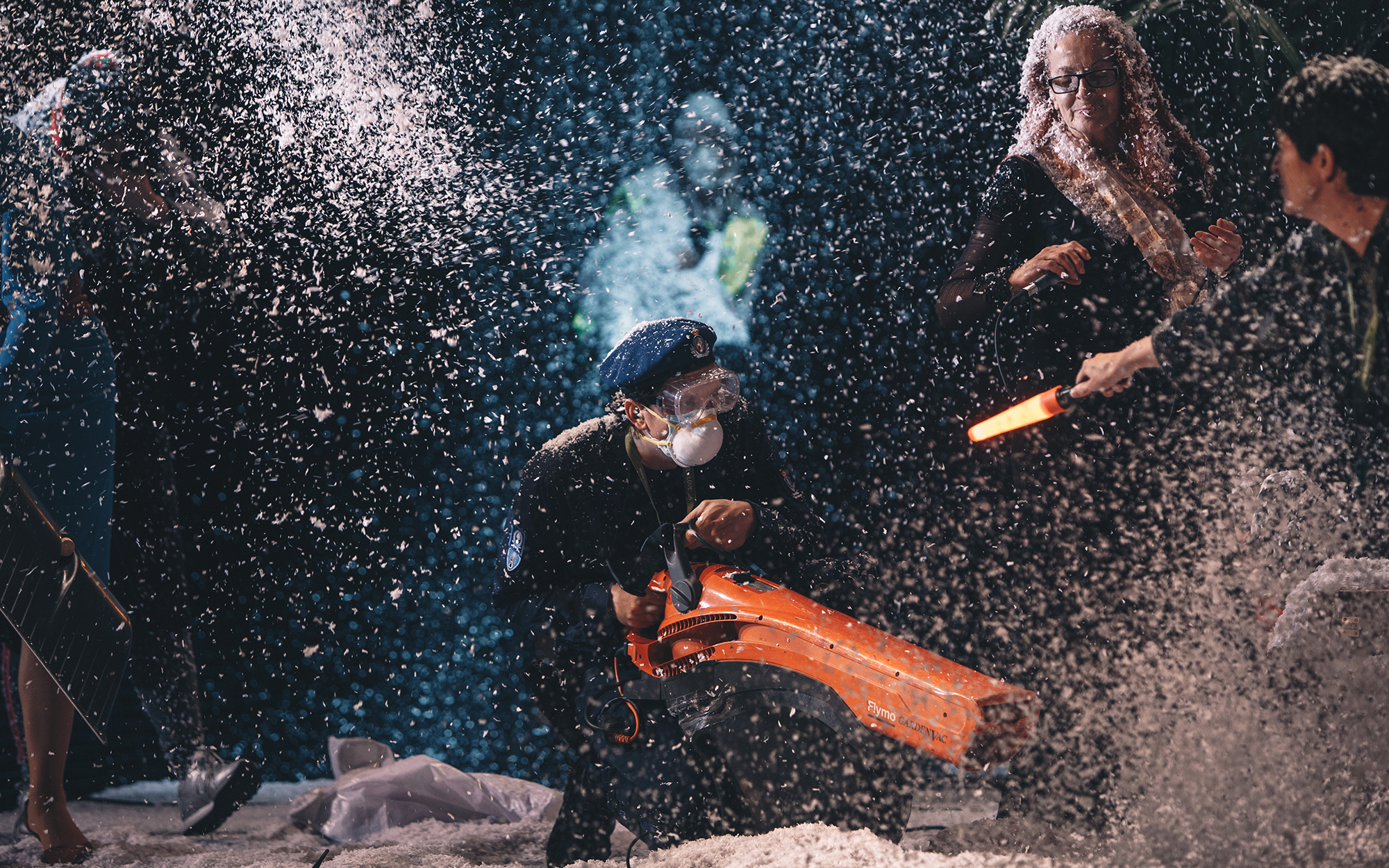 Blue (Jurij Drevenšek) s prozornimi zaščitnimi očali in zaščitno masko na obrazu usmerja pihalnik v kup snega, da se snežinke dvigujejo v zrak. Na desni strani odra stoji Clara (Jožica Avbelj) z mikrofonom v roki, ob njej Rozita (Ana Dolinar Horvat) s sig