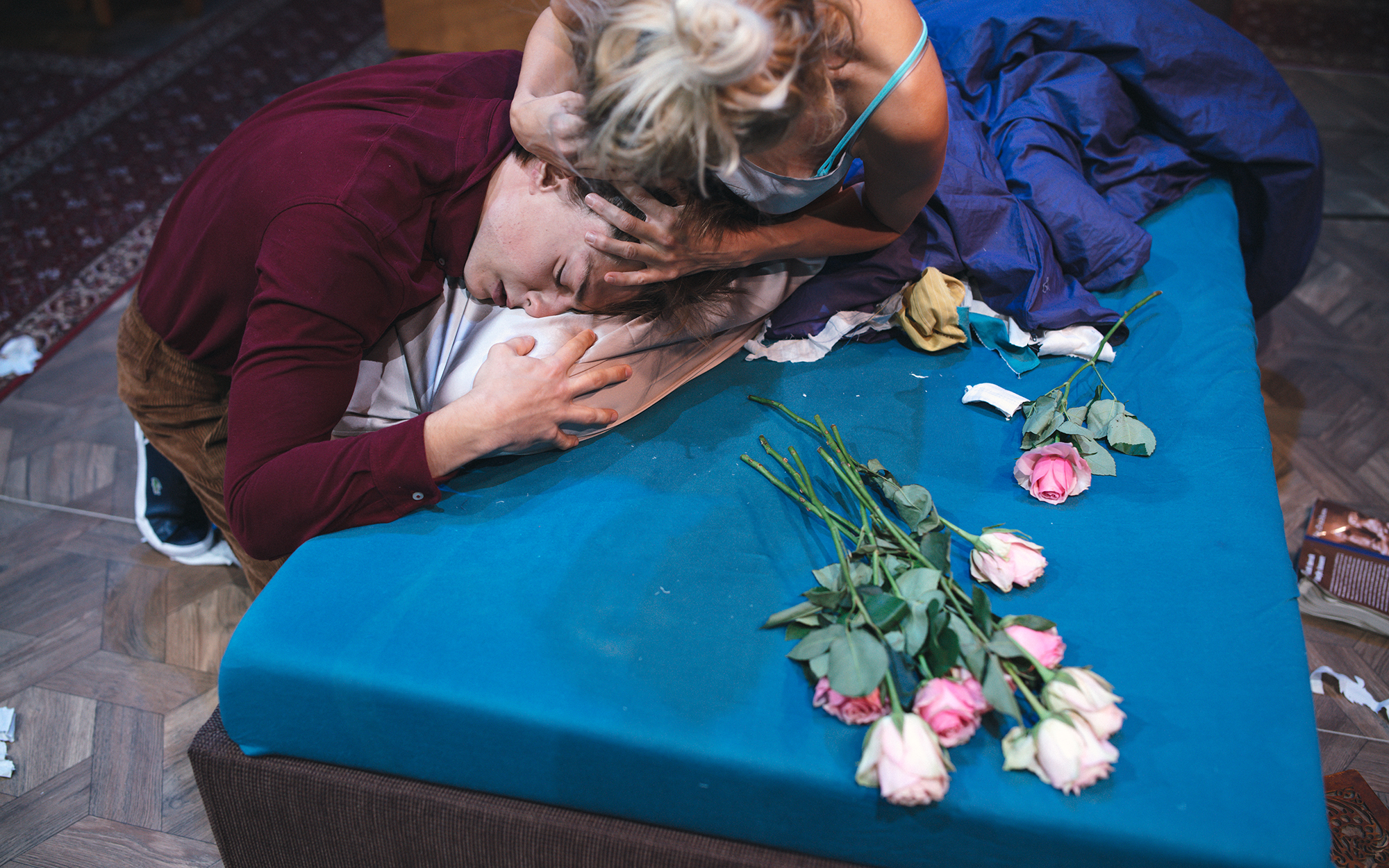Martha (Tjaša Železnik) sedi na postelji in v naročju pestuje Henryjevo glavo (Matej Zemljič). Na postelji je več rožnatih vrtnic. Avtor fotografije: Peter Giodani.