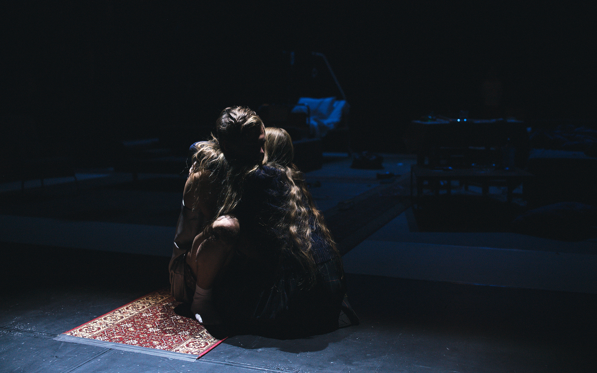 Mia (Ana Pavlin) in Henry (Matej Zemljič) v poltemi čepita na tleh in se objemata. Avtor fotografije: Peter Giodani.