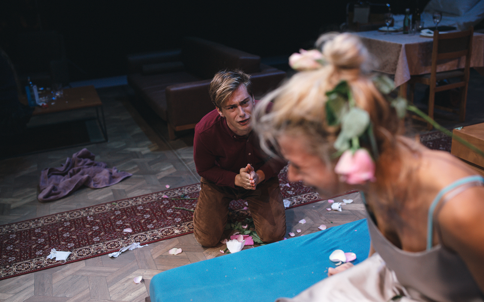 Martha (Tjaša Železnik), ki ima v laseh vrtnice, se joče na postelji, Henry (Matej Zemljič) pa kleči ob njej in jo roti. Avtor fotografije: Peter Giodani.